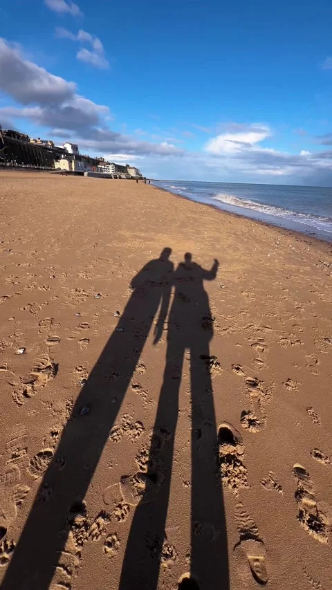 The shadow of a couple is reflected on the sand as they walk along the seaside Stock Footage 292687430