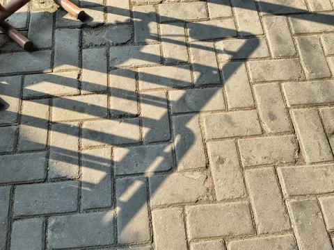 The shadow of a fence on zigzag-patterned paving blocks. Stock Photos
