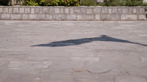 Shadow of a flag waves across a light stone pavement in outdoor sunlight Видео 331305155