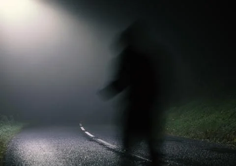 A shadow ghost like figure,  on an empty spooky road at night. Stock Photos