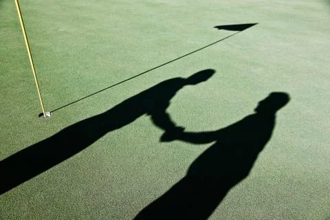 Shadow of golfers and the flag on a green of a golf course. Stock Photos