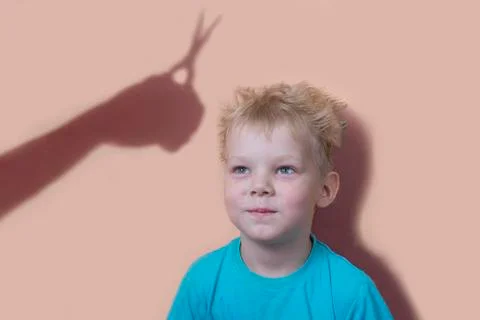 The shadow of a hand with scissors is reflected on the wall.the shaggy boy lo Stock Photos