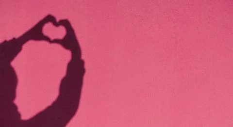 Shadow hands in the shape of a heart on the background of a colored sunny wall Foto stock