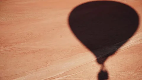 Shadow of a hot air balloon on a red orange dry land on a sunny summer day Stock Footage 265789862