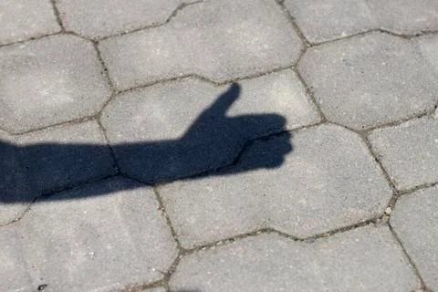 Shadow of human arm and hand with thumb-up success gesture on gray pavement l Stock-Fotos