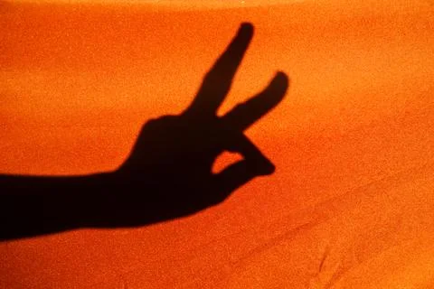 Shadow of a human hand showing peace sign on bright orange fabric 스톡 사진