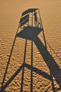 Shadow of lifeguard tower on sandy beach, with silhouette of lifeguard obse.. Stock Photos