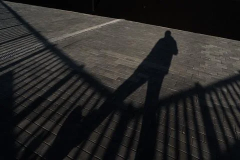 Shadow of a man and a fence on the sidewalk Stock Photos