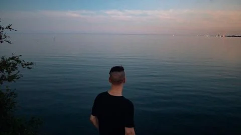 The shadow of a man is contemplating and looking into the lake at sunset Stock-Fotos