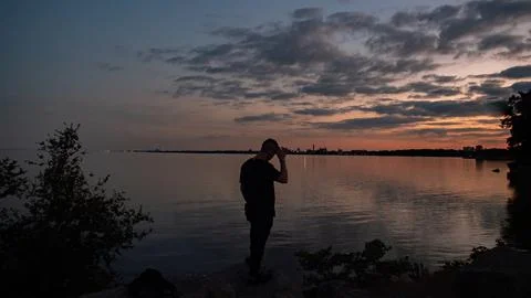 The shadow of a man is contemplating and looking into the lake at sunset Stock-Fotos