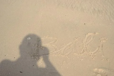 The shadow of a man on a light brown beach sand that says Bali. Stock Photos