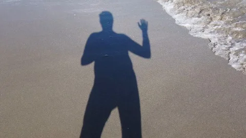 Shadow of a man in the sand. A man holds a camera and waves his hand. 스톡 동영상 124133865