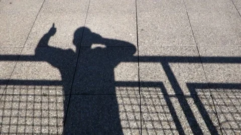 The shadow of a man waving on the stone pavement behind the fence Stock Footage 172383992