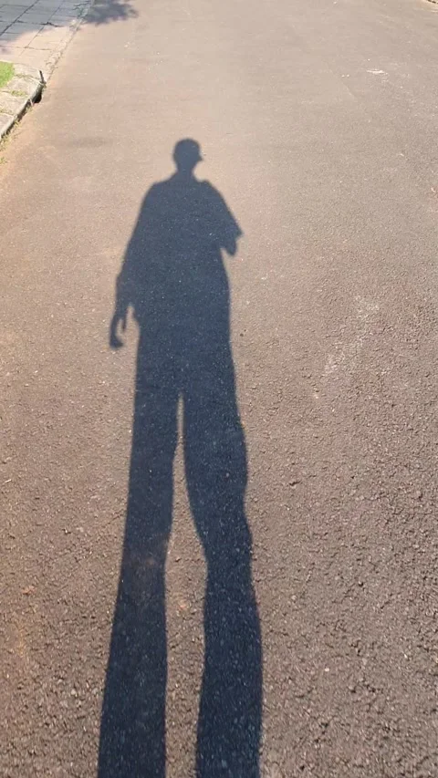 The shadow of a man wearing hat walking.on asphalt road Stock Footage 279996435