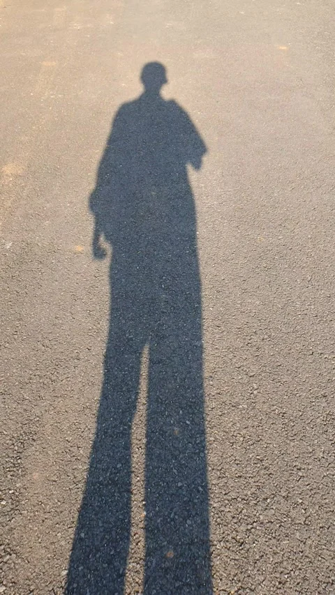The shadow of a man wearing hat walking.on asphalt road Stock Footage 279996441