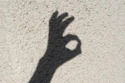 The shadow of a man's hand on the wall shows an okay gesture. Stock Photos