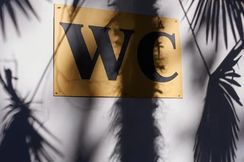 The shadow of a palm tree falls on a white wall with a yellow sign Stock Photos