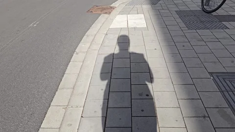 Shadow of a person on a paved city sidewalk near the road during the day Stock Footage 341902408