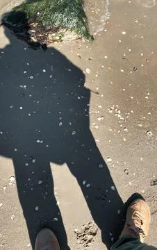 Shadow of person standing on a sandy beach with shallow water and rocks cov.. Stock Photos