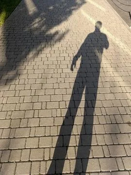A shadow of a person walking down a brick sidewalk Stock Photos