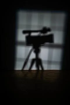 Shadow of a professional video camera on a tripod on the wall in a dark studio Stock Photos