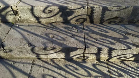 Shadow on stone stairs made of slabs cast by the curved pattern of wrought iron Stock Footage 233488811