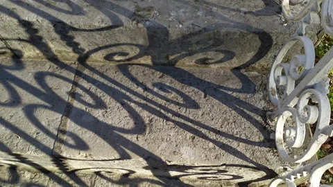 Shadow on stone stairs made of slabs cast by the curved pattern of wrought iron Stock Footage 233490482