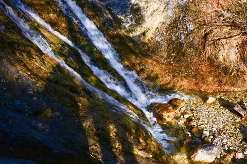 In the shadow, the stream of the waterfall flows along the steep rocks Stock Photos