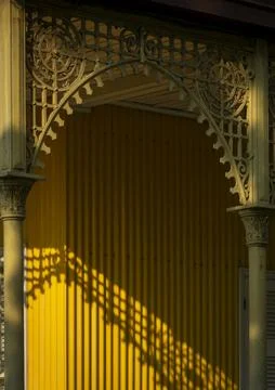 Shadow of a tree branch falls across the yellow wall beneath an arched iron.. Stock Photos