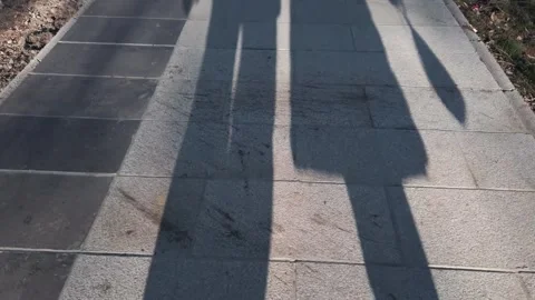 Shadow of two individuals couple walking on a sunlit tiled pavement at sunris Stock Footage 326003754