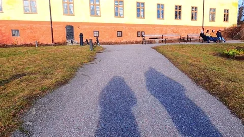 The shadow of two people walking up the path to the colorful building where Vídeos de archivo 297061341