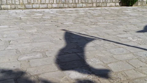 Shadow of waving flag on cobblestone street in bright sunlight captured over Stock Footage 319970386