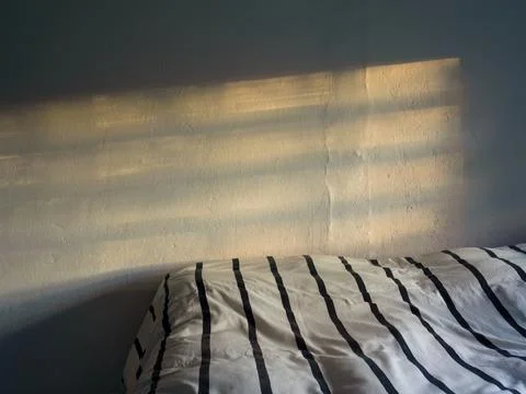 The shadow of a window frame and the light of the sunset above a bed untidy c Foto stock
