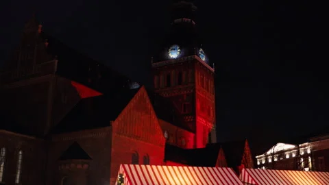 Shadowed church tower with vibrant rooftops, Empty plaza under glowing bulbs and Stock Footage 325349129