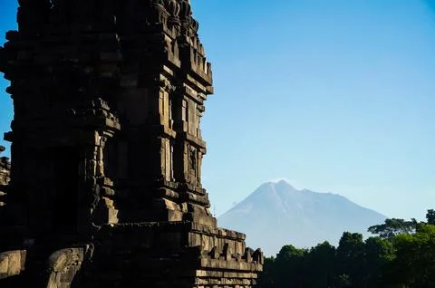 Shadowed Prambanan Temple tower frames distant Mount Merapi beneath a clear.. 스톡 사진