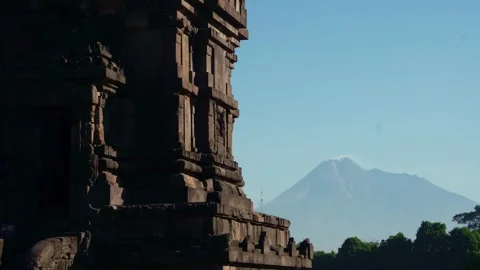 Shadowed Prambanan tower frames distant Mount Merapi beneath clear blue ski.. Stock Footage 341544025