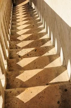 Shadows and light play on an aged stone staircase with geometric patterns. Stockfoto's