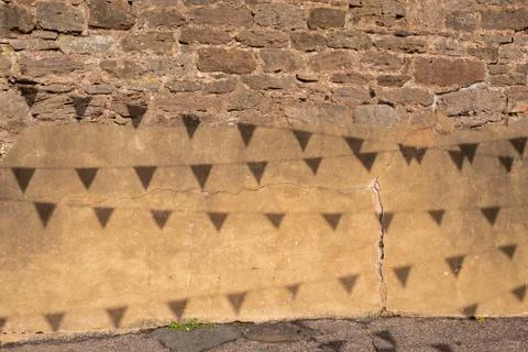 Shadows from bunting hanging overhead create a pattern on a crumbling brick w Stock Photos