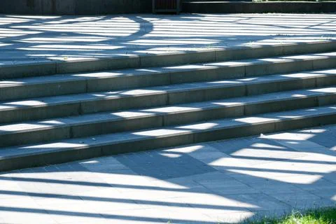 Shadows dance across steps in a sunlit urban park Stock Photos