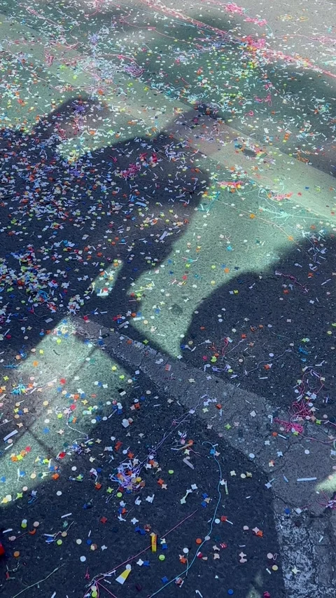Shadows of people celebrating on confetti covered asphalt during a carnival Stock Footage 345035478