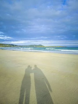 Shadows of two human standing on the sandy beach Stock Photos