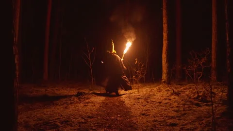 In a shadowy forest, a wizard carries a torch as he makes his way through the Video stock 306323094