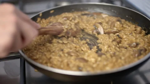 Shaking and mixing a pan full with mushroom risotto with a wooden spoon. Stock Footage 134697229