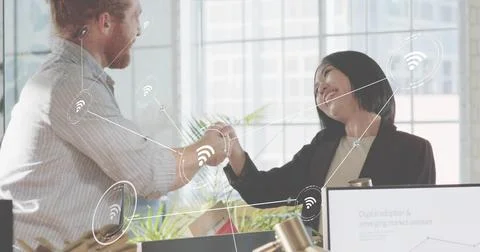Shaking hands two colleagues in office wearing business attire, with monitor Stock Photos
