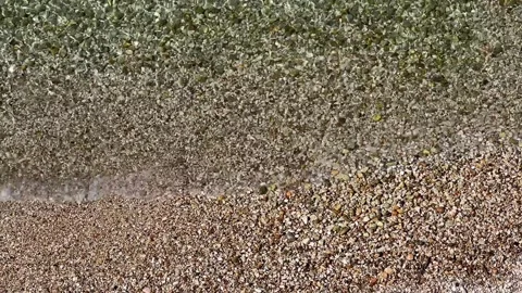 Shallow clear water waves over brown pebble sand shore viewed from above Stock Footage 243442055