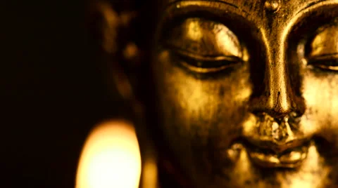 Shallow focus closeup of rotating face of a golden candlelit Buddha figure Stock Footage