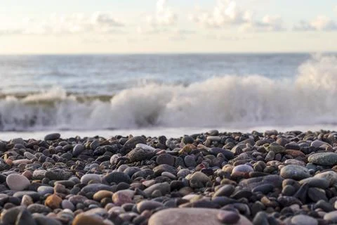Shallow focus view of multi-colored beach pebbles with a crashing sea wave .. Stock Photos