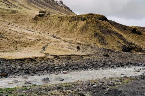 A shallow mountain river flows against a mountain with yellow grass in Iceland. 스톡 사진