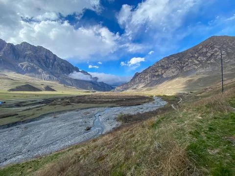 A shallow mountain river runs between two rocky mountains Foto stock