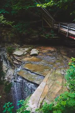 Shallow river flowing over cliffs next to walking bridge Stock Photos